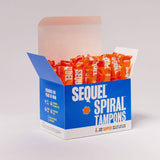 An open blue and white Sequel™ The Spiral™ Tampons box reveals several upright, individually wrapped orange tampons with helical grooves. The box contains 32 Super tampons for distraction-free periods, all set against a plain background.