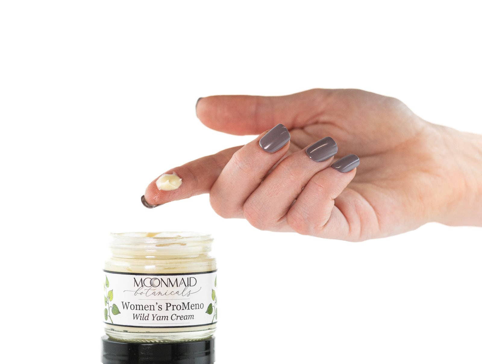 A hand with gray-painted nails holds a dollop of cream above an open jar labeled ProMeno Women's Wild Yam Cream against a white background.
