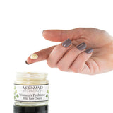 A hand with gray-painted nails holds a dollop of cream above an open jar labeled ProMeno Women's Wild Yam Cream against a white background.