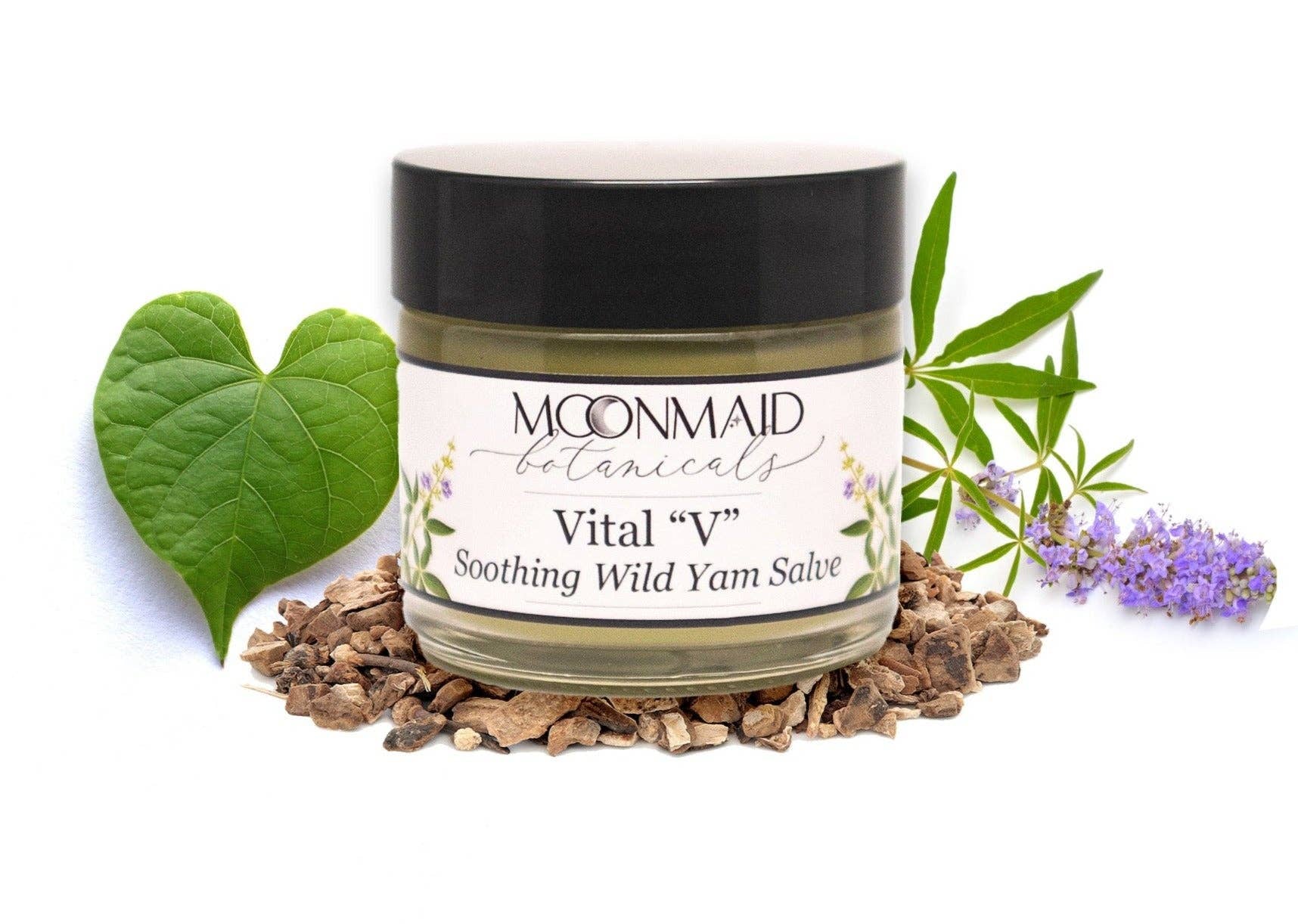 A jar of Vital "V" Wild Yam Salve rests on dried roots, alongside a green heart-shaped leaf and delicate purple flowers, with lush foliage in the background.