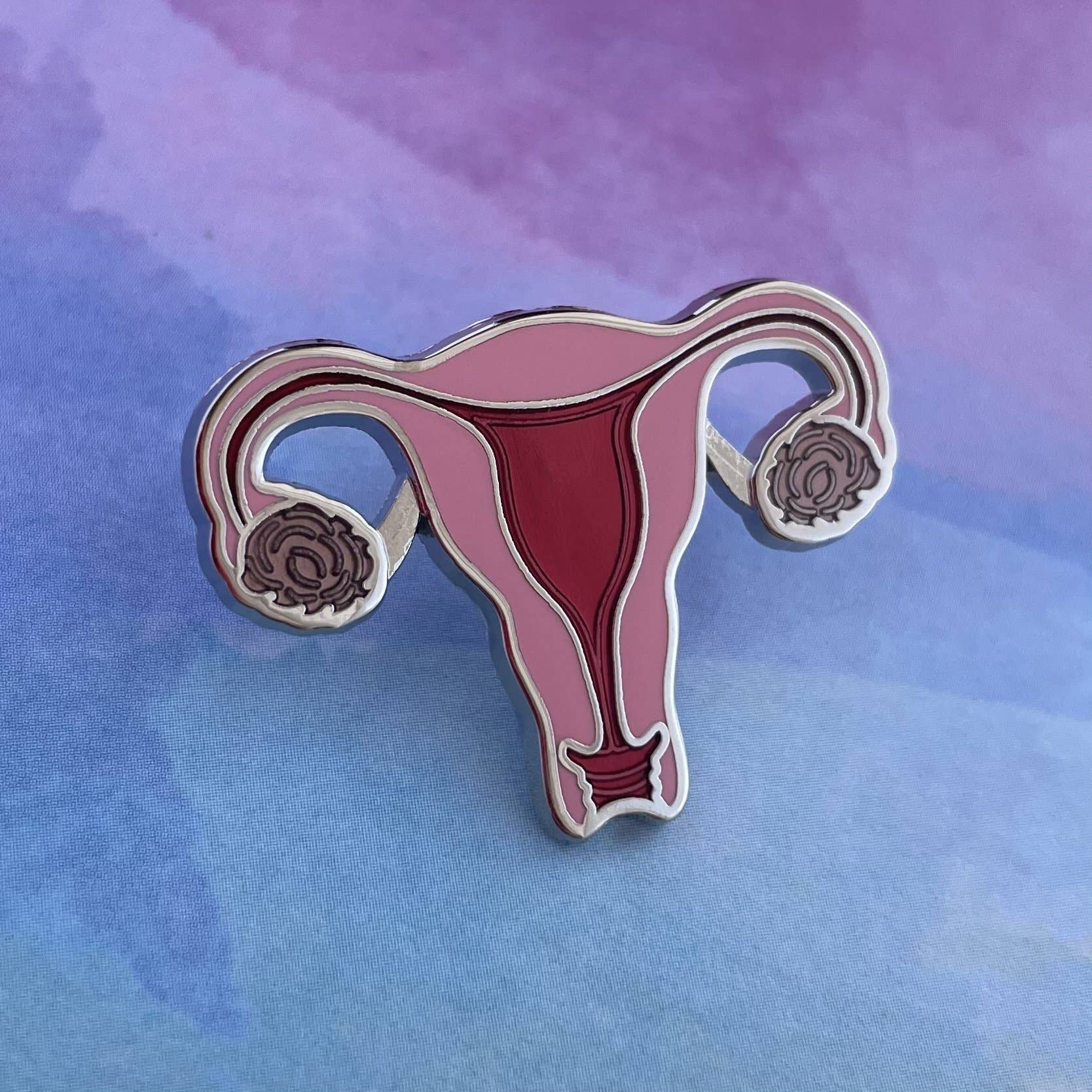 The OB/GYN Pin Pack features a colorful enamel uterus pin with detailed fallopian tubes and ovaries, shown on a purple-blue gradient—perfect for anatomy and OB GYN pin collections.