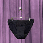 A pair of Period Swim Bottoms - Bikini Cut hangs on a hanger with clips in front of a purple velvet curtain.