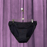 A pair of Period Swim Bottoms - Bikini Cut hangs on a hanger with clips in front of a purple velvet curtain.