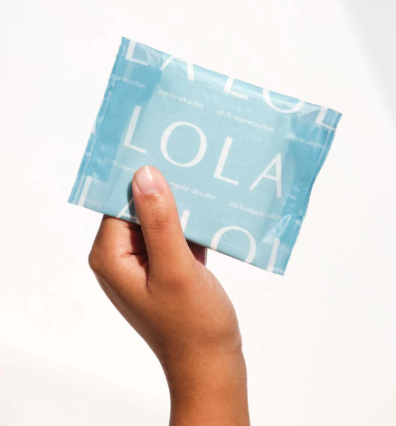A hand holds a light blue packet of Lola 20ct Ultra Thin Pads w/ Wings, Regular, featuring the brand name in white letters on the packaging and offering reliable leak protection.