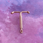 The OB/GYN Pin Pack features a copper intrauterine device (IUD) with extended arms on a soft purple and pink watercolor background—perfect for OB GYNs or anatomy pin collectors.