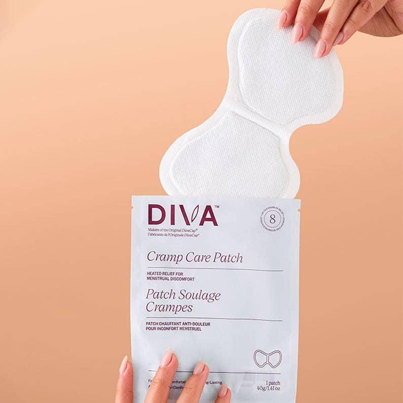 A person holds The Cramp Care Patch package with a white self-heating patch partly removed, against a peach background. The packaging highlights effective relief for menstrual cramp discomfort.