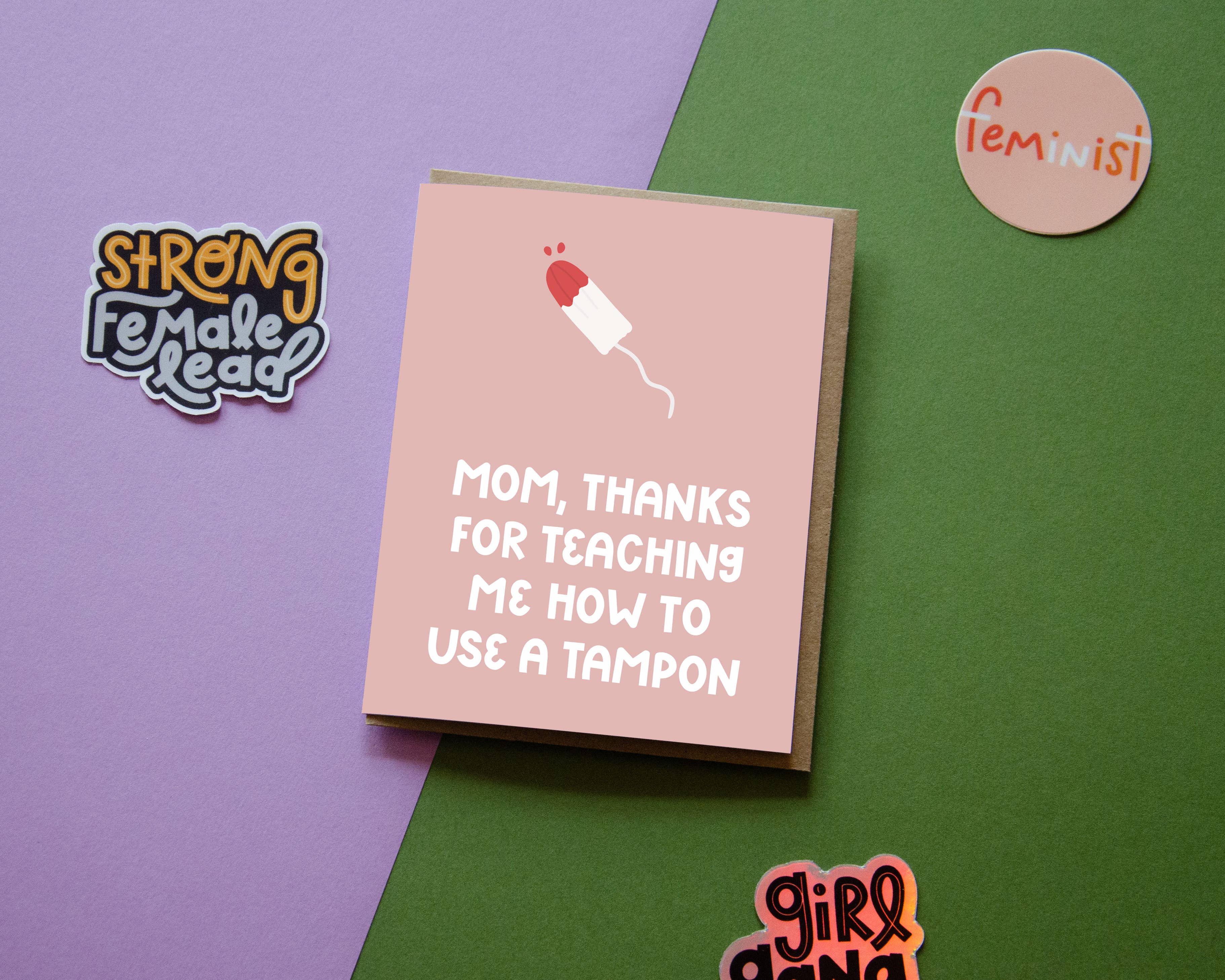 The Thanks for Teaching Me To Use a Tampon Card features hand-lettered text on a pink and green background with a funny illustration, plus nearby stickers that read Strong Female Lead, Feminist, and girl gang.