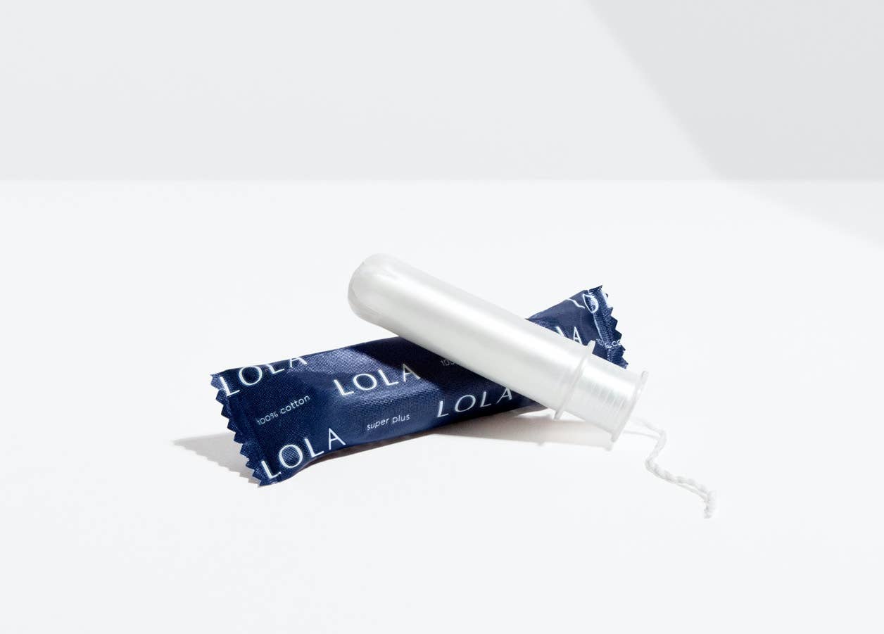 A wrapped and an unwrapped Lola 20ct Super Plus Tampon, made with organic cotton and a BPA-free applicator, are shown on a white surface against a plain white background.