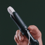A hand displays the DAME Reusable Tampon Applicator with a white tampon inside, showcasing its use against a dark green background.