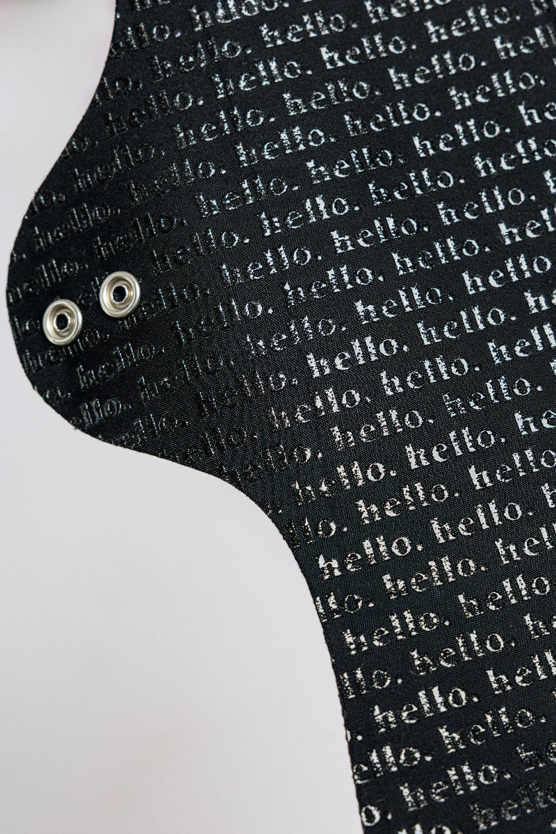 Black cloth pad with 'hello' text pattern on a white background and with metal snap wings