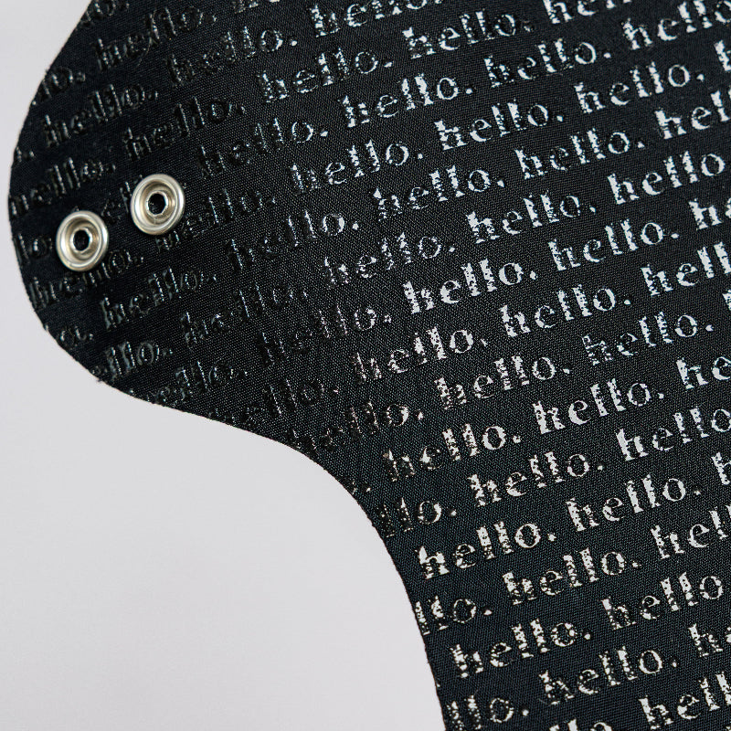 Black cloth pad with 'hello' text pattern on a white background and with metal snap wings
