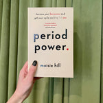 A hand with black nail polish holds "Period Power: Harness Your Hormones & Cycle Benefits" in front of green curtains, highlighting how understanding your hormones can help you make the most of your menstrual cycle.