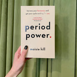 A hand with black nail polish holds "Period Power: Harness Your Hormones & Cycle Benefits" in front of green curtains, highlighting how understanding your hormones can help you make the most of your menstrual cycle.
