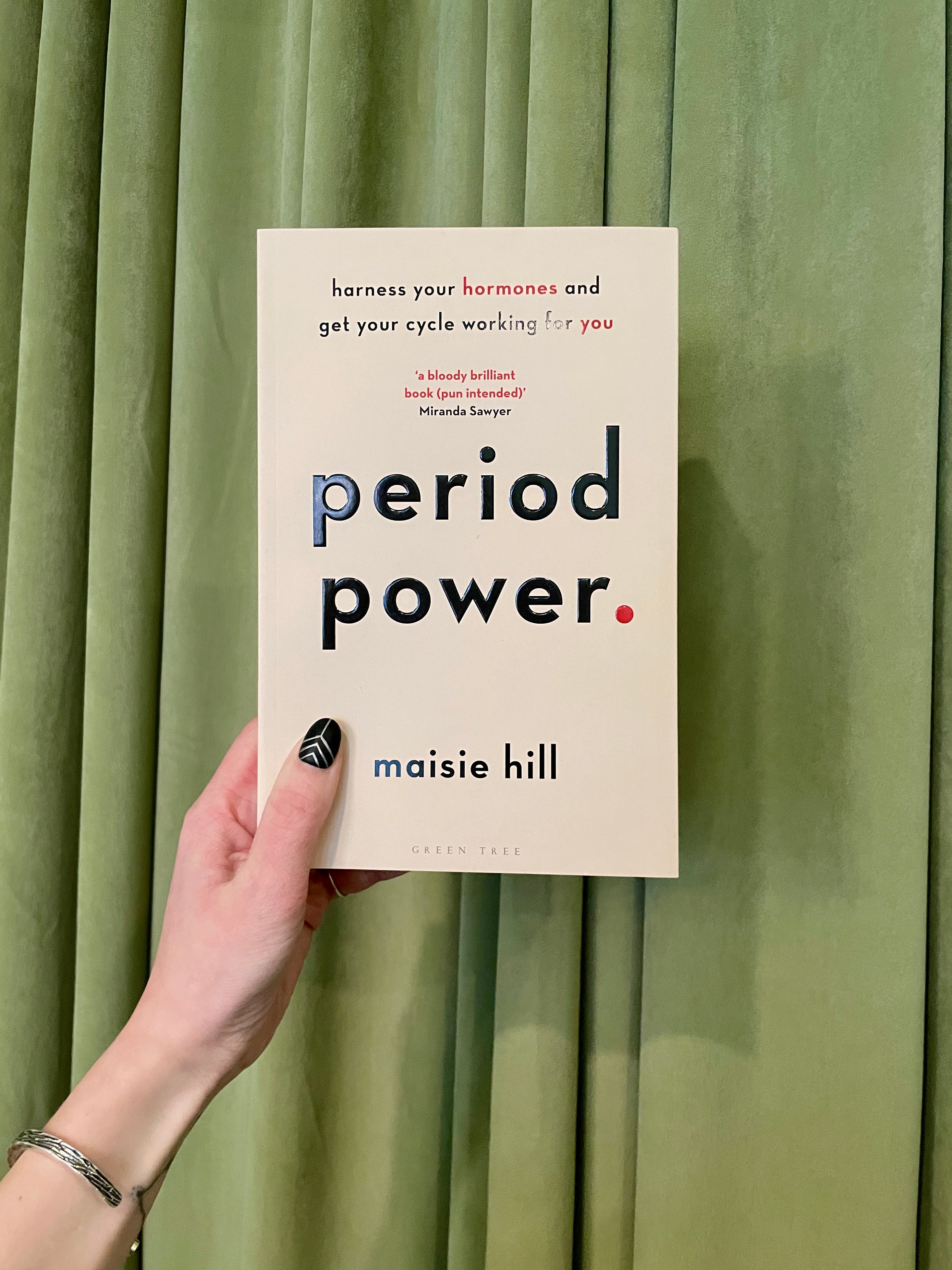 A hand with black nail polish holds "Period Power: Harness Your Hormones & Cycle Benefits" in front of green curtains, highlighting how understanding your hormones can help you make the most of your menstrual cycle.
