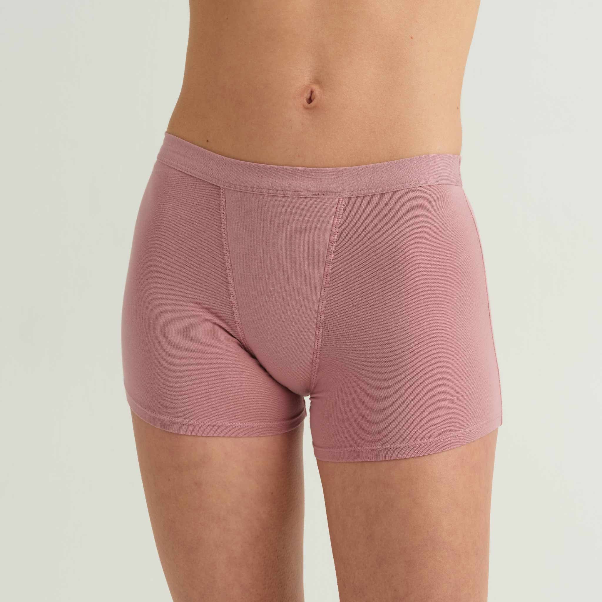 A person models the Saalt Wear Leakproof Cotton Sleep Short in pink and a beige crop top, standing against a plain light background. The image is cropped to show only the torso and upper thighs.