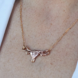 A close-up of a person wearing the Bronze Uterus Necklace by Bang-Up Betty—a striking bronze pendant on a chain, shown against light skin and a white garment from the creator known for bold statement jewelry.