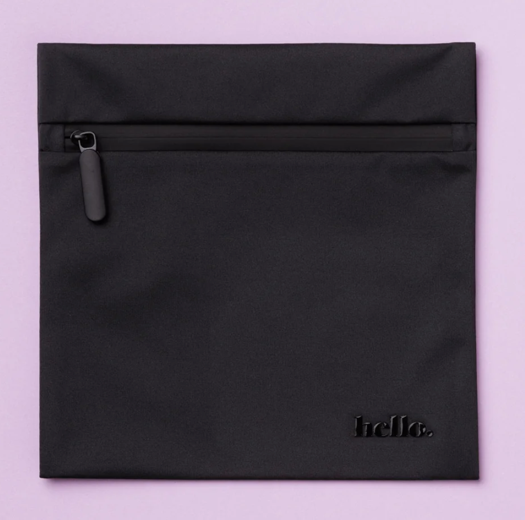 The Hello Wet Bag is a black, waterproof storage bag with a matte finish and “hello.” embossed in lowercase letters at the bottom right, shown against a light purple background.