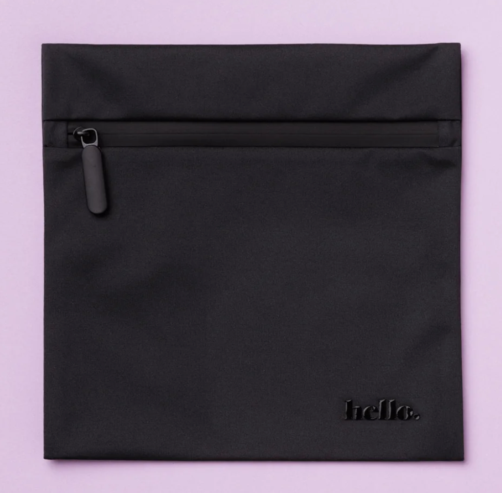 The Hello Wet Bag is a black square wet bag featuring a top zipper pocket and "hello." embossed in the lower right corner, shown against a light purple background.