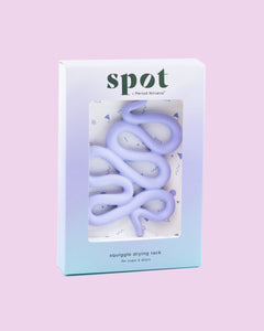 Spot is a pastel purple squiggly drying rack for cups and discs that doubles as a stylish menstrual disc holder, showcased in gradient blue and white packaging labeled Spot by Period Nirvana, set against a light pink background.
