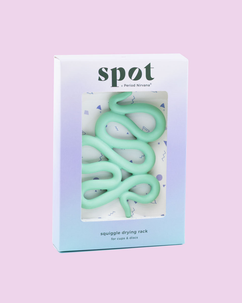 A pastel-colored box labeled Spot holds a mint green, squiggly silicone menstrual cup and disc holder, displayed on a light purple background.