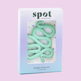 A pastel-colored box labeled Spot holds a mint green, squiggly silicone menstrual cup and disc holder, displayed on a light purple background.