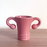 The Shooterus - Uterus Shot Glass is a pink ceramic cup shaped like a uterus, complete with fallopian tube handles—a playful novelty perfect for celebrating milestones like menopause or hysterectomy with humor.