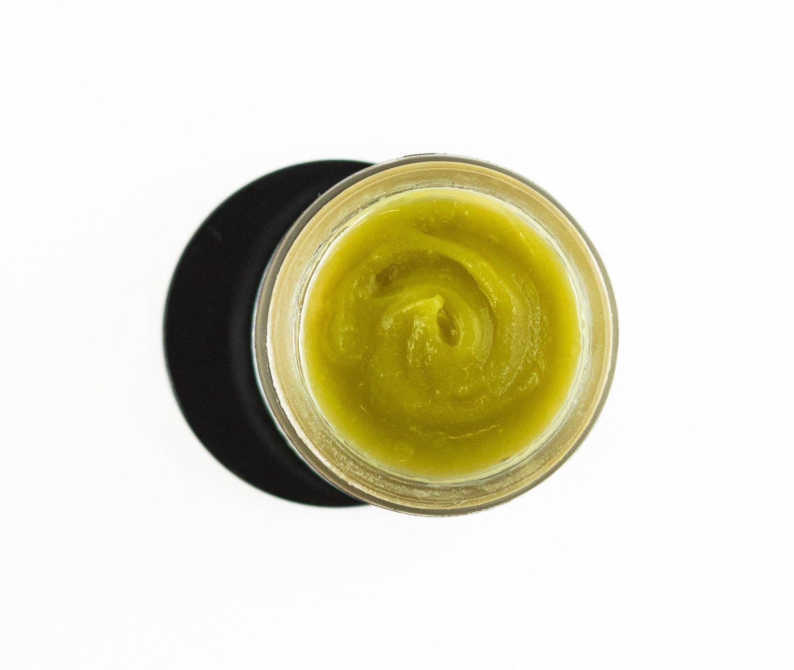 A top-down view of an open jar of Vital "V" Wild Yam Salve, a smooth greenish-yellow balm ideal as a natural intimate moisturizer or for vaginal dryness relief, set on a white background with a black circular shadow beneath the jar.