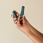 A person's hands hold the DAME Reusable Tampon Applicator—a small, dark green, cylindrical object with a cap—against a neutral beige background, highlighting this eco-friendly and hygienic period care product.