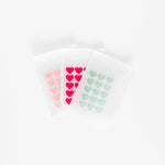 Three translucent plastic pouches of Big Hug Breakout Pimple Patches, each with a sheet of pink and teal heart-shaped hydrocolloid patches, are displayed on a white background.