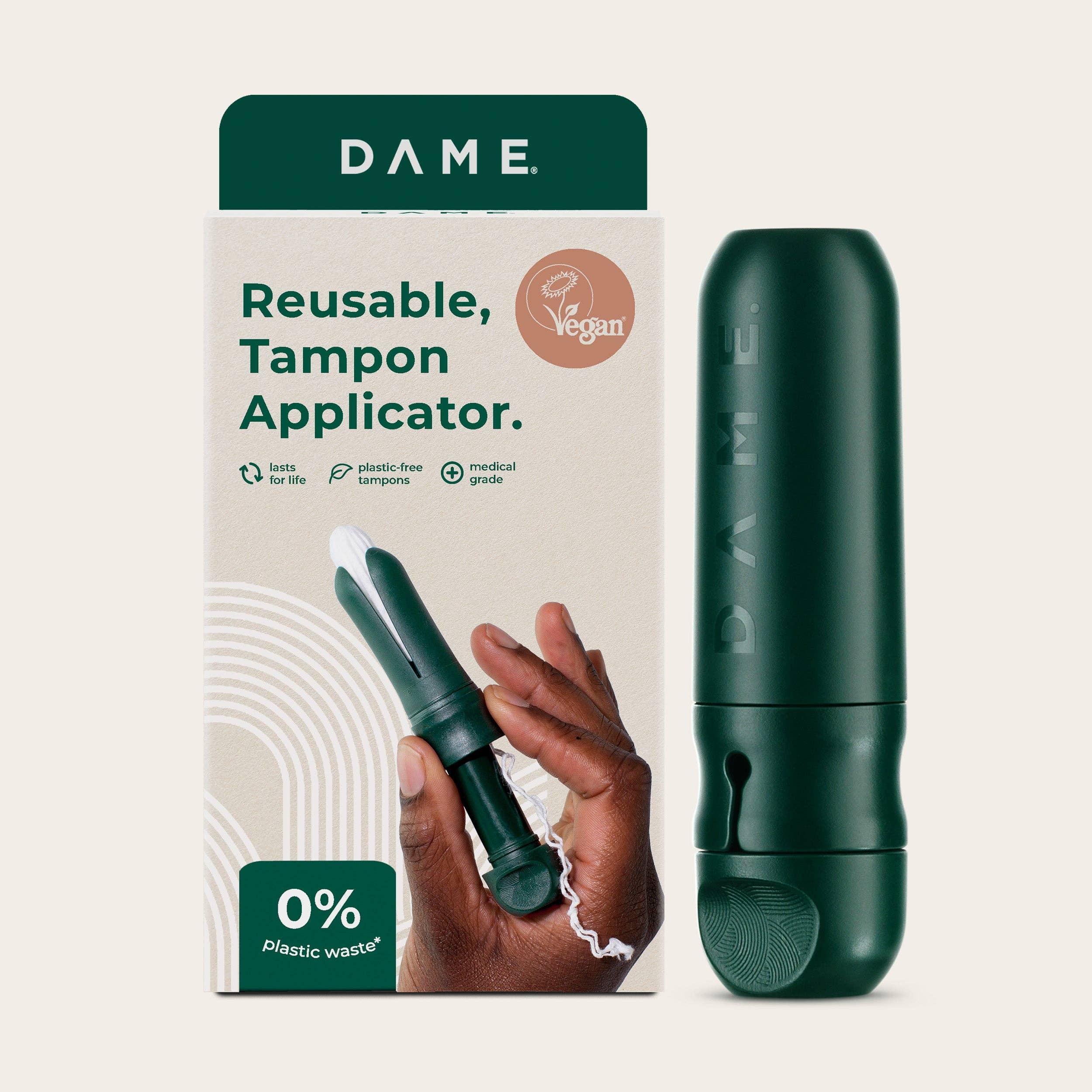 A hand holds the DAME Reusable Tampon Applicator, a dark green, medical-grade, vegan applicator for a plastic-free period. The packaging reads: “DAME. Reusable Tampon Applicator. Vegan. 0% plastic waste!”—designed to last for life.