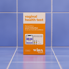 A box of Winx Health Vaginal Health Test & Treat rests on blue tiles. The orange and white packaging notes it's an at-home yeast infection test with two tests, plus info about same-day treatment options.