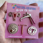 A hand holds the OB/GYN Pin Pack, which features five pins: a uterus, a speculum, a fetus in womb, an IUD, and a cervix anatomy pin with "AT YOUR CERVIX" text.