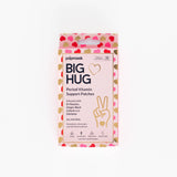 A rectangular box of Big Hug Period Support Vitamin Patches with a pink, red, and gold heart pattern, natural ingredients text, and a hand making a peace sign design for gentle PMS relief.