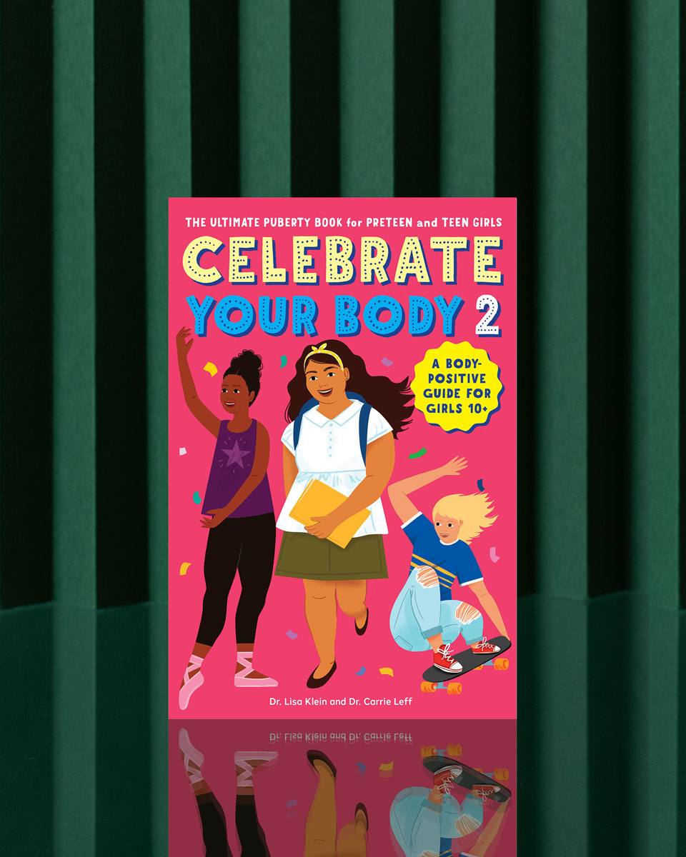 The book "Celebrate Your Body 2" stands upright against a green striped background, featuring three smiling, diverse girls—one dancing, one with books, and one skateboarding—on its cover.