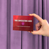 A hand with red-painted nails holds a box labeled Red Tribe Period Conversation Cards in front of purple curtains. The box features five categories with 41 fun questions—ideal for growing up discussions and great conversations!.