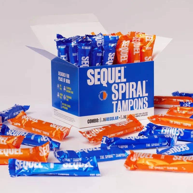 An open box of Sequel™ The Spiral™ Tampons reveals blue and orange individually wrapped tampons with helical grooves, scattered on a white surface. The bold packaging showcases Sequel’s promise of reliable, distraction-free period protection.