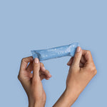 Two hands hold a box of Lola 20ct Super Tampons, featuring BPA-free applicators, against a solid light blue background.