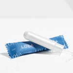A Lola 20ct Super Tampon made from white organic cotton with a BPA-free applicator sits on its blue wrapper, displayed against a plain white background.