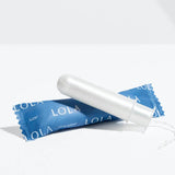 A Lola 20ct Super Tampon made from white organic cotton with a BPA-free applicator sits on its blue wrapper, displayed against a plain white background.
