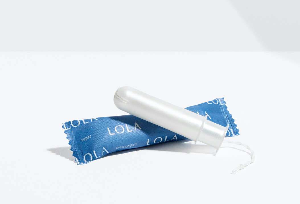 A Lola 20ct Super Tampon made from white organic cotton with a BPA-free applicator sits on its blue wrapper, displayed against a plain white background.