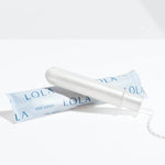 A Lola 20ct Light Tampon with a BPA-free applicator rests beside its light blue LOLA wrapper on a white surface, casting a soft shadow.