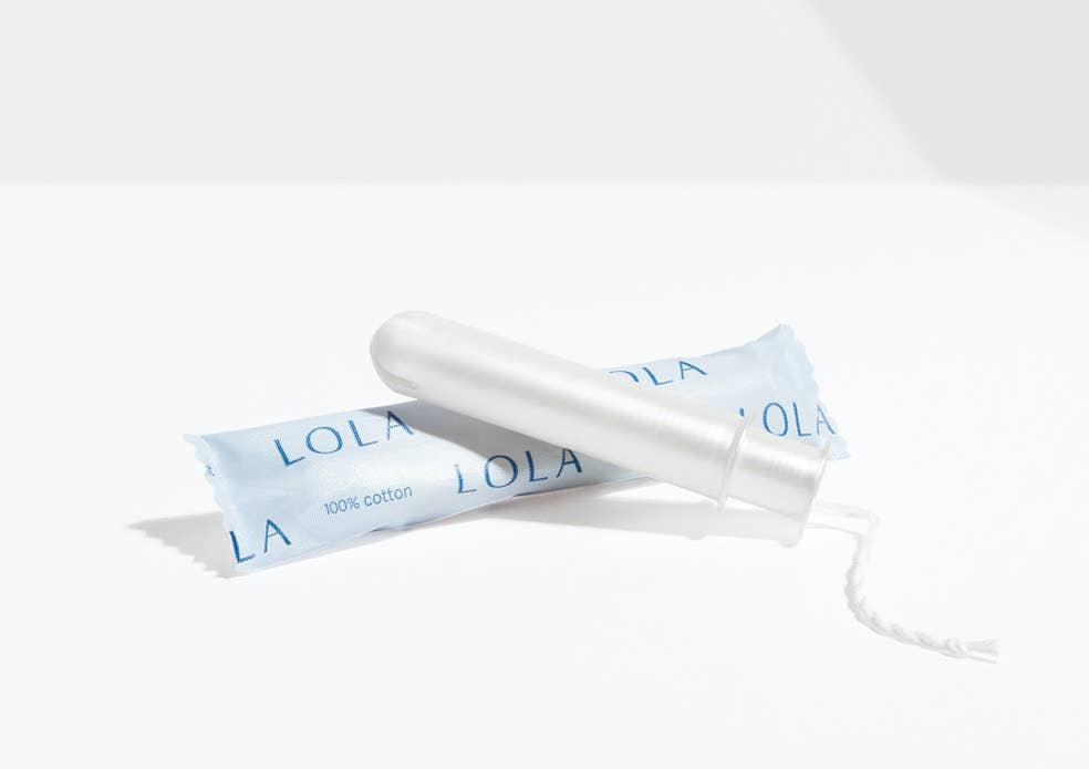 A Lola 20ct Light Tampon with a BPA-free applicator rests beside its light blue LOLA wrapper on a white surface, casting a soft shadow.