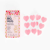 A box labeled Big Hug Period Support Vitamin Patches sits beside six pink heart-shaped patches in clear blister packaging. Decorated with pink and red hearts, the box offers PMS relief using convenient vitamin patches.