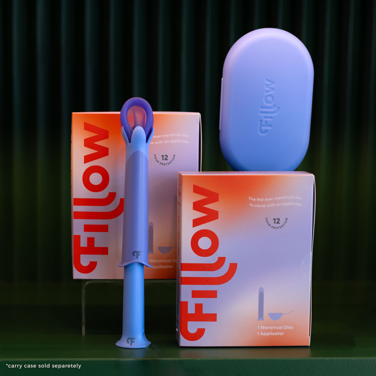 Two Fillow Disc and Applicator kits with orange and white boxes, a blue applicator in front, and a blue carry case beside them are shown on a dark green background. Note: the blue carry case is sold separately—an alternative to tampons.