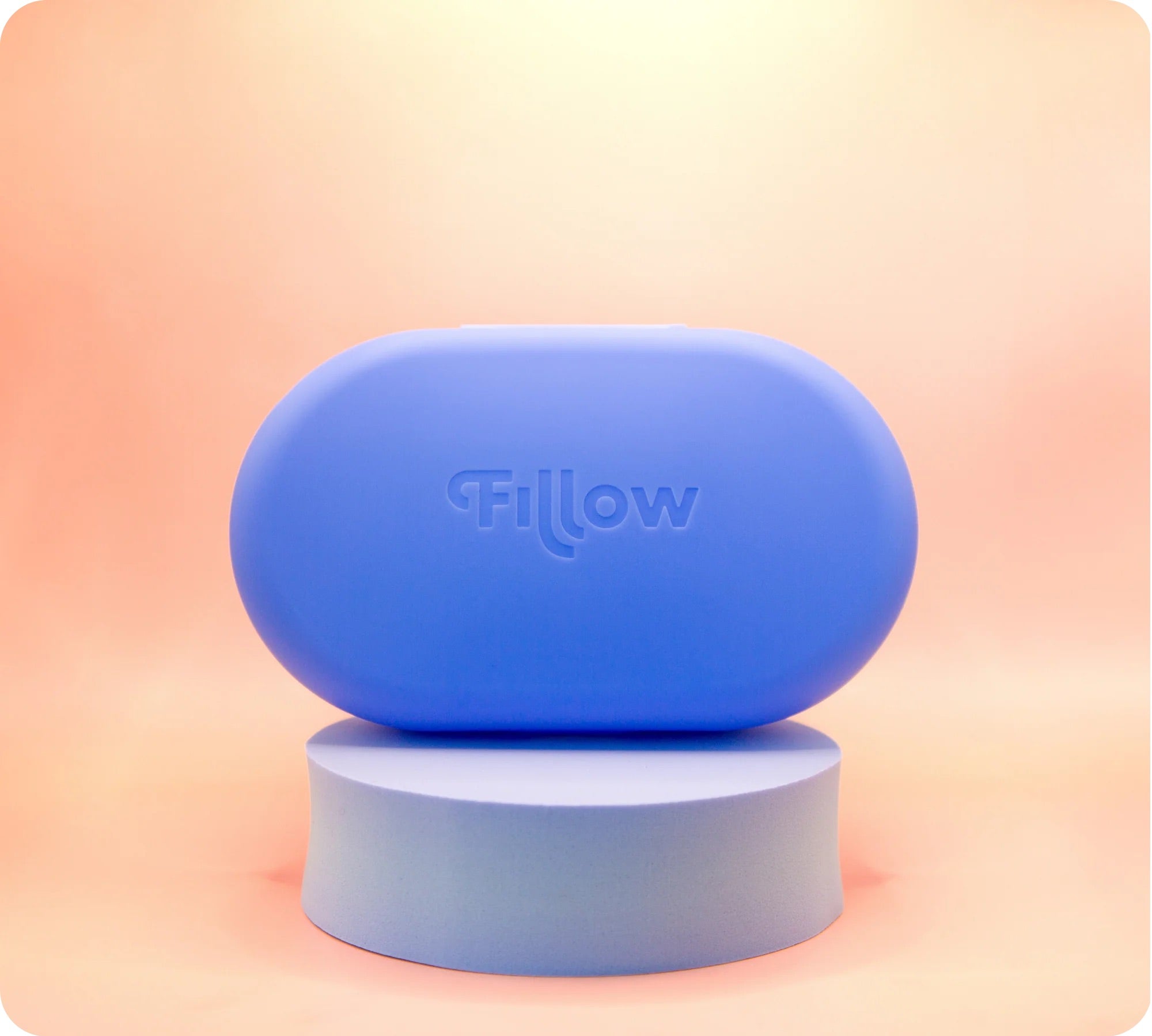 The Fillow Carry Case, a rounded blue case with "Fillow" embossed, sits on a matching pedestal against a peach gradient background, designed as the perfect disc and applicator case for stylish travel storage.