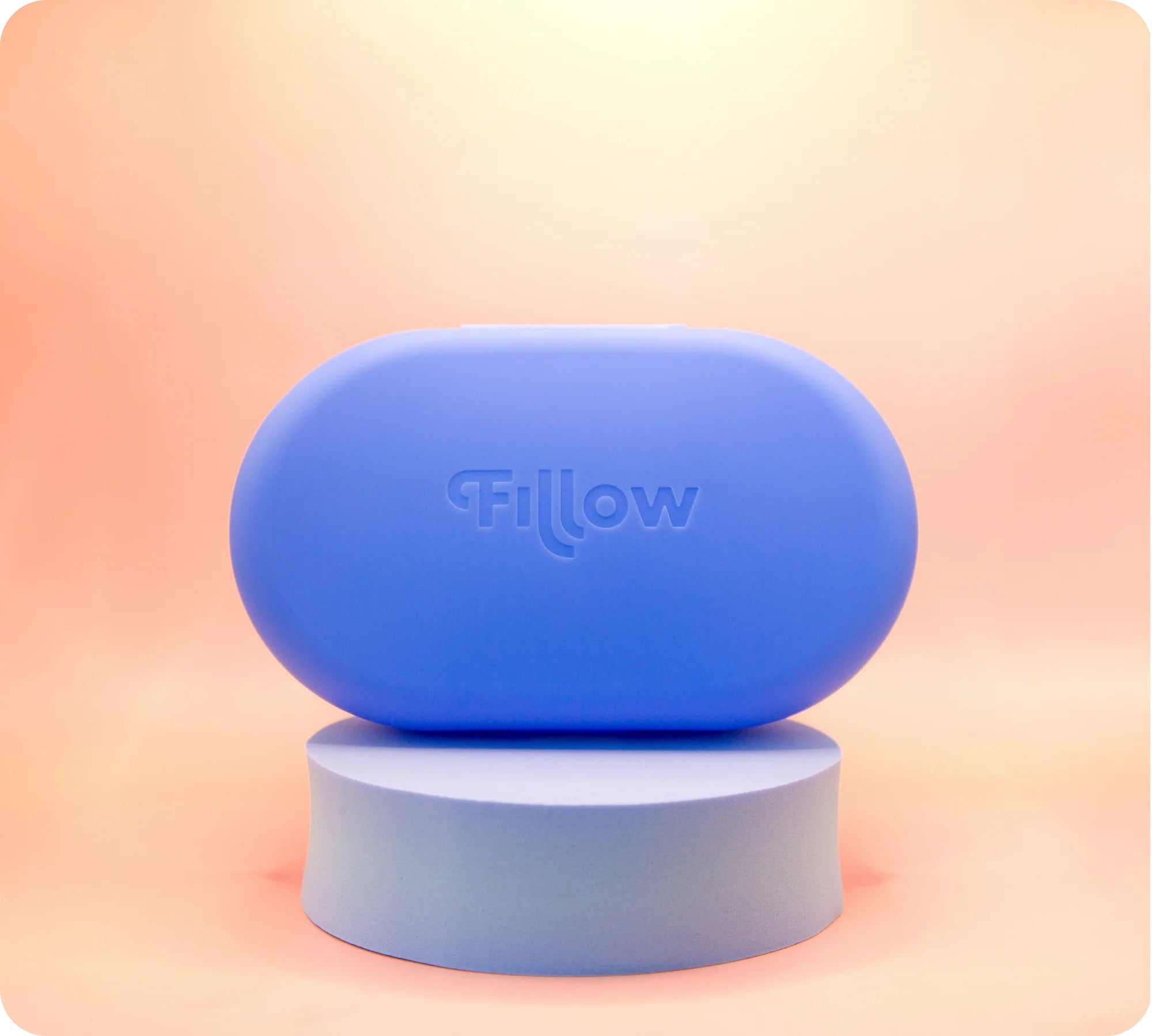 The Fillow Carry Case, a rounded blue case with "Fillow" embossed, sits on a matching pedestal against a peach gradient background, designed as the perfect disc and applicator case for stylish travel storage.