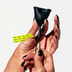 A hand with black nail polish holds a black Flex Cup, a menstrual cup featuring a pull-tab stem for easy removal—making it the only beginner-friendly cup that removes like a tampon.