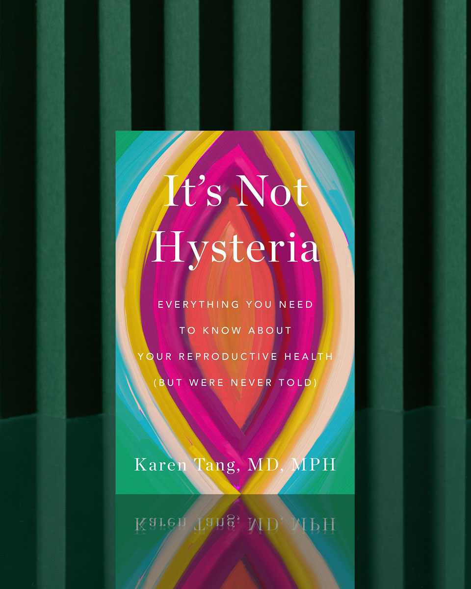 A vibrant copy of It's Not Hysteria: Everything You Need To Know About Reproductive Health stands upright on a green-striped background, its cover displaying bold abstract shapes in pink, orange, yellow, green, and blue.