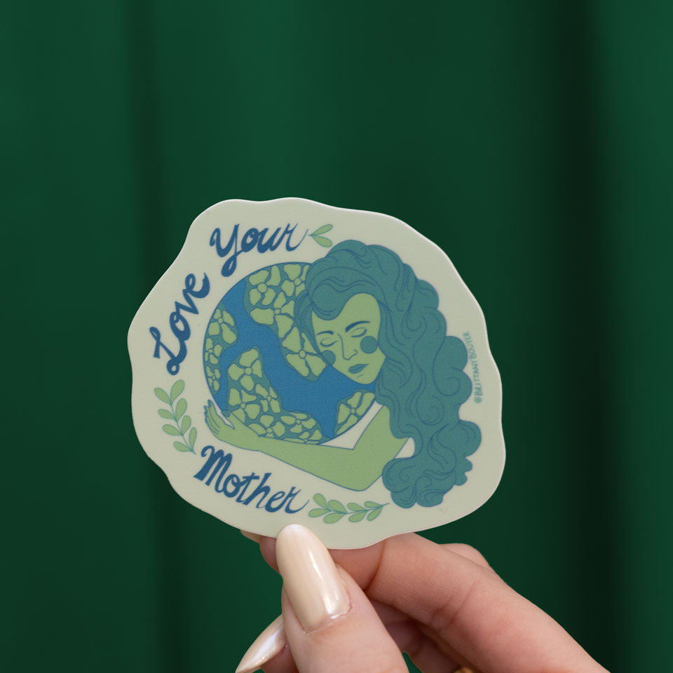 Hand holding a 'Love Your Mother' sticker with a green background