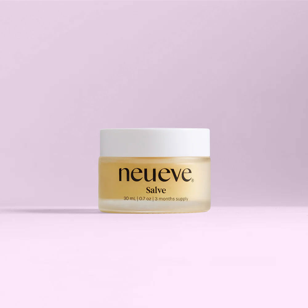 A small jar of NeuEve Salve - Moisturize & Soothe Vulvar Dryness, with a white lid and clear container, rests on a light pink background. The 30 ml (1 oz) label notes it’s a 3-month supply for relief from vulvar dryness and atrophy.